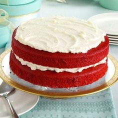 a red velvet cake with white frosting sitting on a plate next to silverware