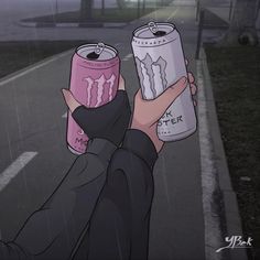 a person holding two cans of monster energy drink in the middle of a street at night