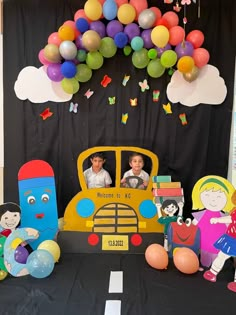 a table topped with balloons and toys next to a yellow school bus filled with kids