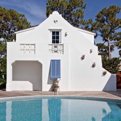 a white house with blue shutters next to a swimming pool in front of it