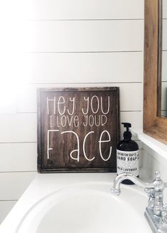 a bathroom sink with a wooden sign above it that says hey you love your face