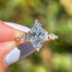 a woman's hand holding an engagement ring with three pear shaped diamonds