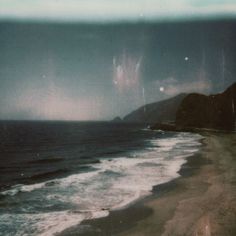 an old photo of the ocean with waves coming in to shore and mountains in the distance