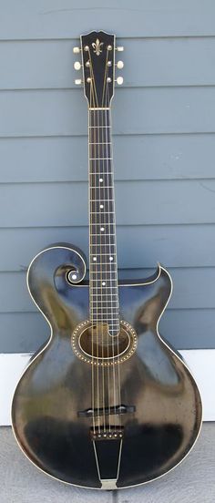 an acoustic guitar is sitting on the ground in front of a blue wall and gray siding