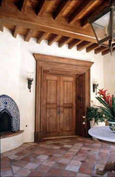 a cat sitting on the floor in front of a wooden door and brick patio with potted plants