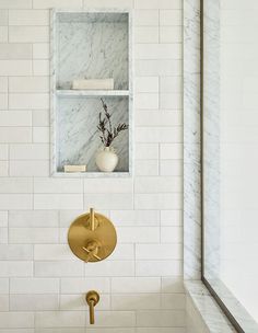 a white tiled bathroom with gold faucet and marbled shower head, shelves above the bathtub