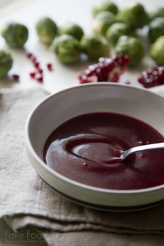 a white bowl filled with red sauce next to brussel sprouts and cranberries