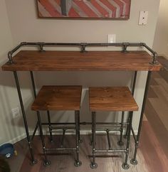 a wooden table with metal legs and stools in front of a painting on the wall