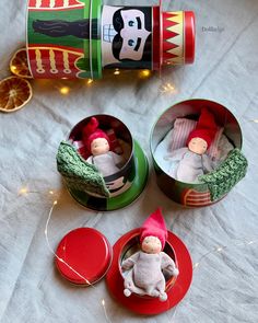 three tins with christmas decorations and two small dolls in them on a table next to an orange slice