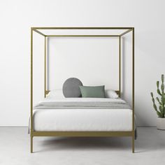 a white bed with a gold frame and green pillows on the bottom, next to a potted cacti