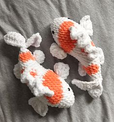 three small knitted koi fish laying on top of a gray blanket with white and orange accents