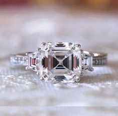 an engagement ring with a fancy diamond center stone on it's side, sitting on top of a table