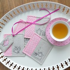 three tea bags and a cup on a white plate with pink ribbon tied around them