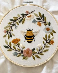 a bee is sitting in the middle of a floral wreath with leaves and flowers on it