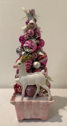 a pink and white christmas tree with ornaments on it's top, sitting in a box