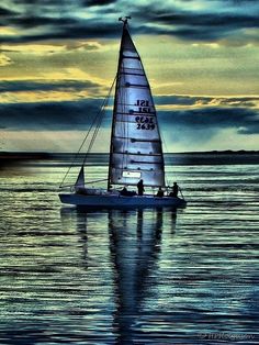 a sailboat is sailing on the water at sunset with clouds in the sky behind it