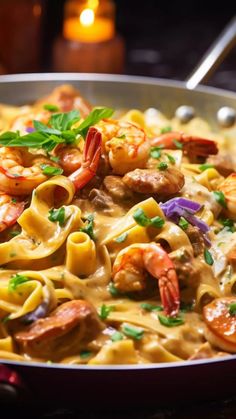 a pan filled with pasta and shrimp on top of a table next to a lit candle