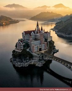 an aerial view of a castle in the middle of water with mountains in the background