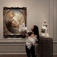 a woman standing in front of a painting with white ruffles on her arms