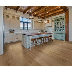 a large kitchen with wooden floors and white cabinets, an island in the middle is surrounded by stools