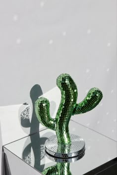 a shiny green cactus sitting on top of a glass table next to a white wall