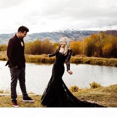 a man standing next to a woman on top of a grass covered field near a lake