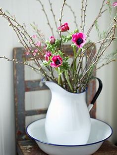 a white pitcher filled with pink flowers on top of a wooden table