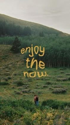 a person standing in a field with the words enjoy the now written on it's side