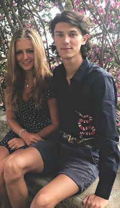 a young man and woman sitting next to each other on a stone bench in front of pink flowers