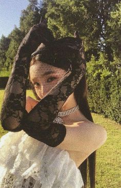 a woman in a white dress holding her hands up to her face while wearing black lace gloves