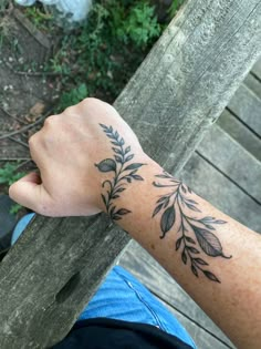 a person with a tattoo on their arm holding onto a wooden fence rail outside in the sun