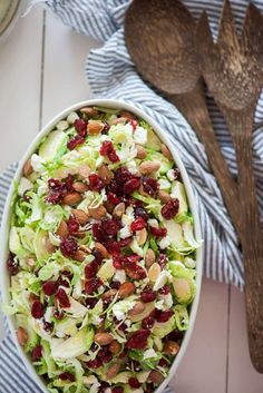 a salad with cranberries and almonds in a bowl next to a wooden spoon