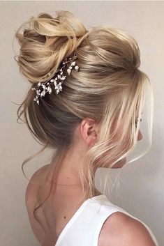 a woman with blonde hair in a messy updo wearing a white top and pearls on her head