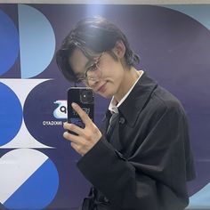 a young man taking a selfie in front of a blue and white background with his cell phone