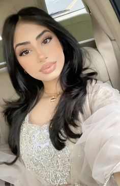 a woman sitting in the back seat of a car wearing a white dress and gold necklace