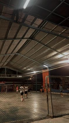 some people are playing soccer in an indoor court at night time with the lights on