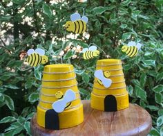 three beehive made out of construction paper on top of a wooden table next to bushes