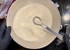 a person mixing flour in a bowl with a whisk on the side and a measuring spoon