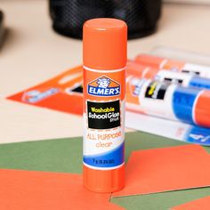 an orange tube of glue sitting on top of some cut out pieces of construction paper