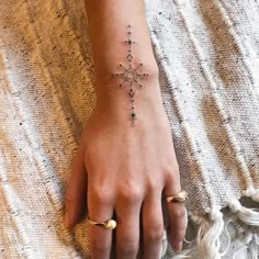 a woman's hand with a cross tattoo on her left wrist and gold rings