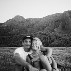 a man and woman are sitting in the grass with mountains in the backgroud