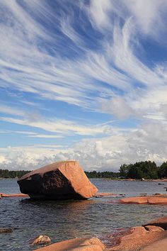 a large rock sitting in the middle of a lake surrounded by rocks and water with trees in the background