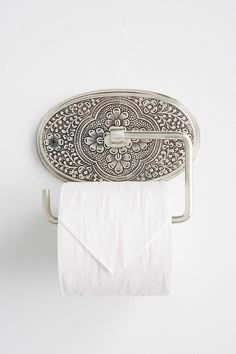 a toilet paper holder with an ornate design on the front and sides, holding a roll of tissue