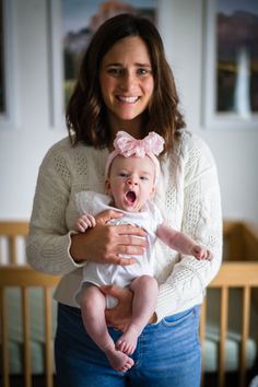 a woman holding a baby in her arms and smiling at the camera with an excited look on her face