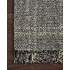 the grey and white checkered wool rug with fringes is on a wooden floor