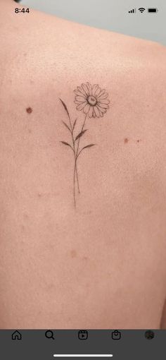 the back of a woman's shoulder with a single flower tattoo on her left side