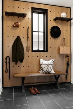 a wooden bench sitting under a window next to a wall with hooks and hats on it