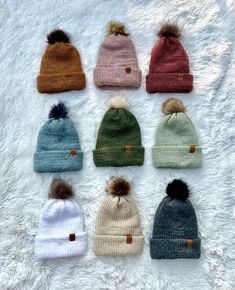 six knit beanies with pom - poms laid out on a white blanket