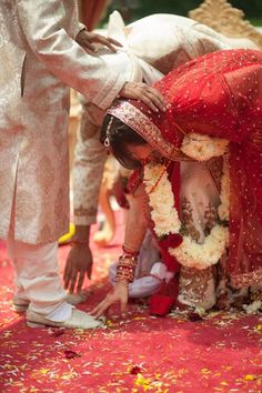 a man kneeling down next to a woman in a red and white wedding dress with flowers on the floor