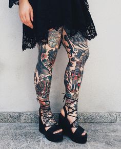 a woman with tattoos on her legs and leggings is standing in front of a wall